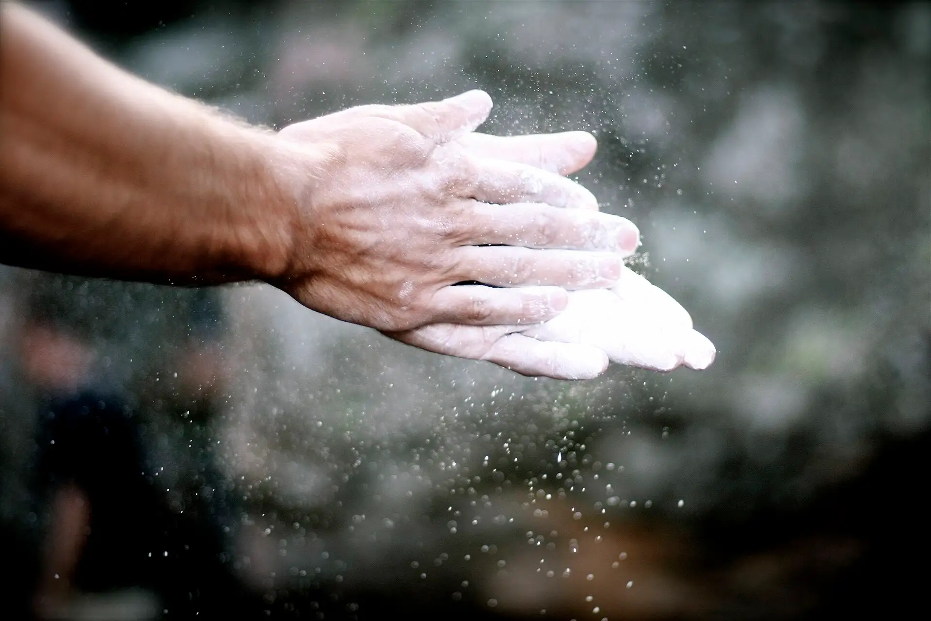 A climber's chalked hands, with chalk dust in the air.
